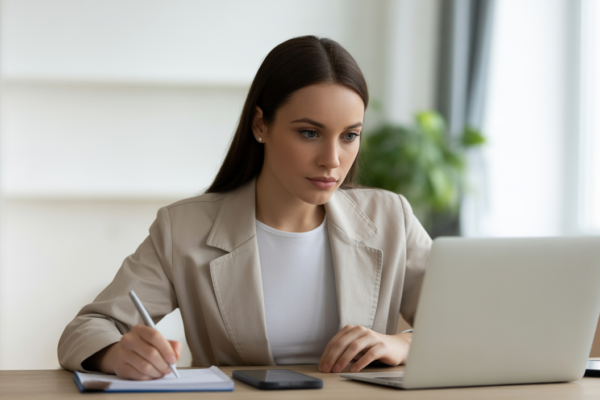 Photorealistic image of a young professional woman focused on taking an online exam on a laptop in a clean white workspace showing remote proctoring concept